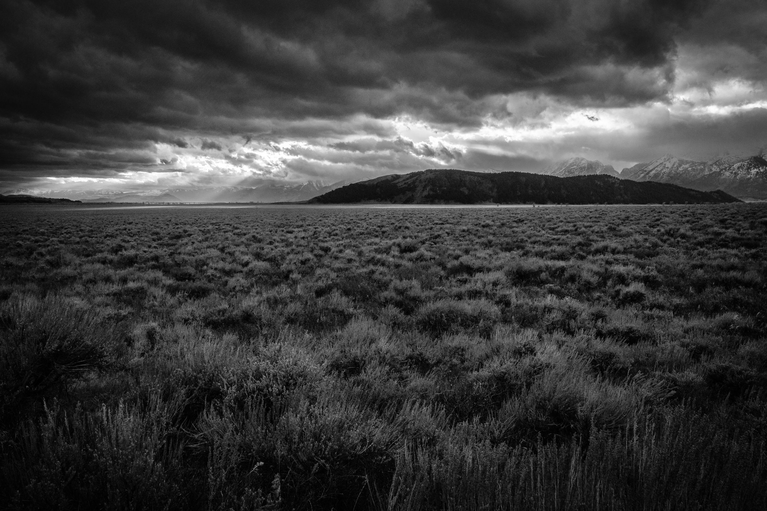 Antelope Flats under storm clouds, at sunset. In the background, Blacktail Butte, and sunset light breaking through the clouds.